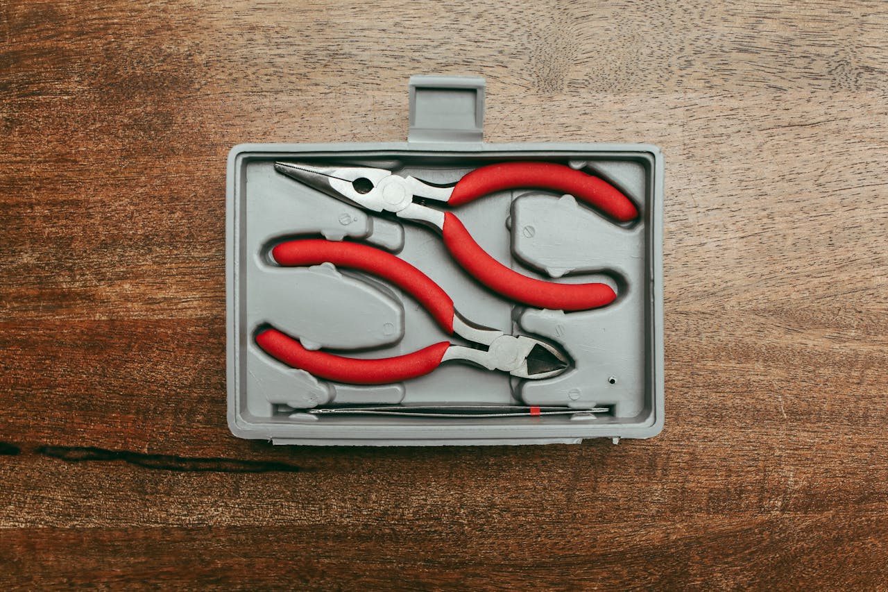 Top view of a red handled pliers set in a box on a wooden surface.
