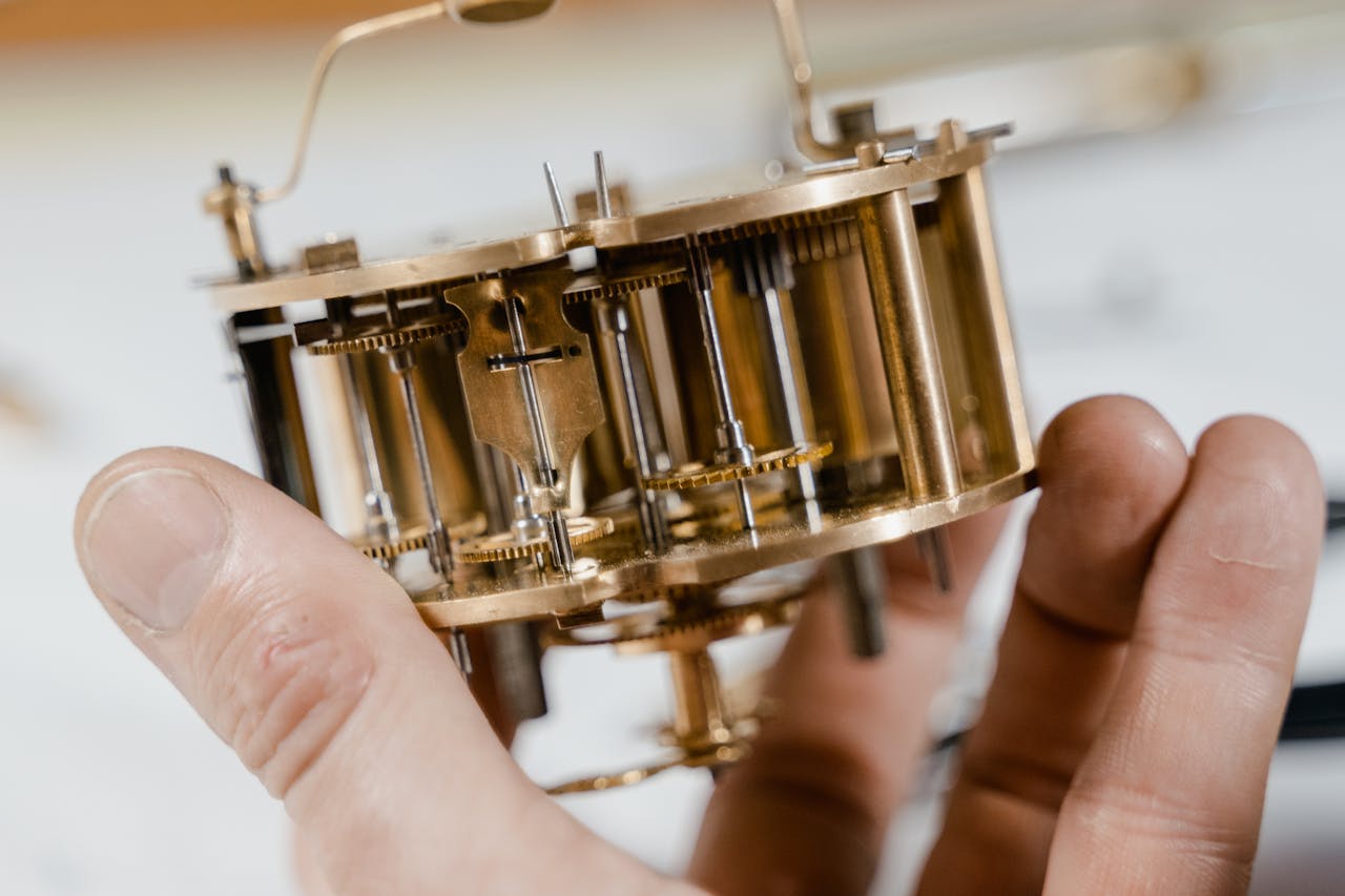 Close-up of a vintage clock mechanism held by hands, showcasing intricate details.